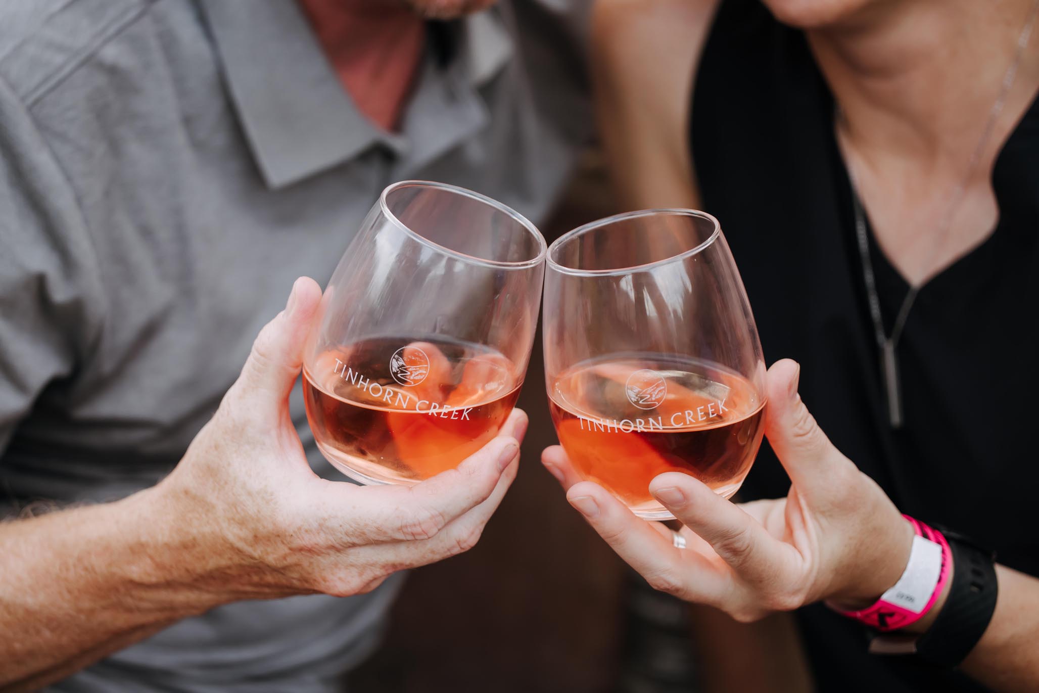 Two people clinking glasses of rosé wine, each glass labeled with "Tinhorn Creek." The individuals' faces are not visible, focusing on the gesture of the toast.